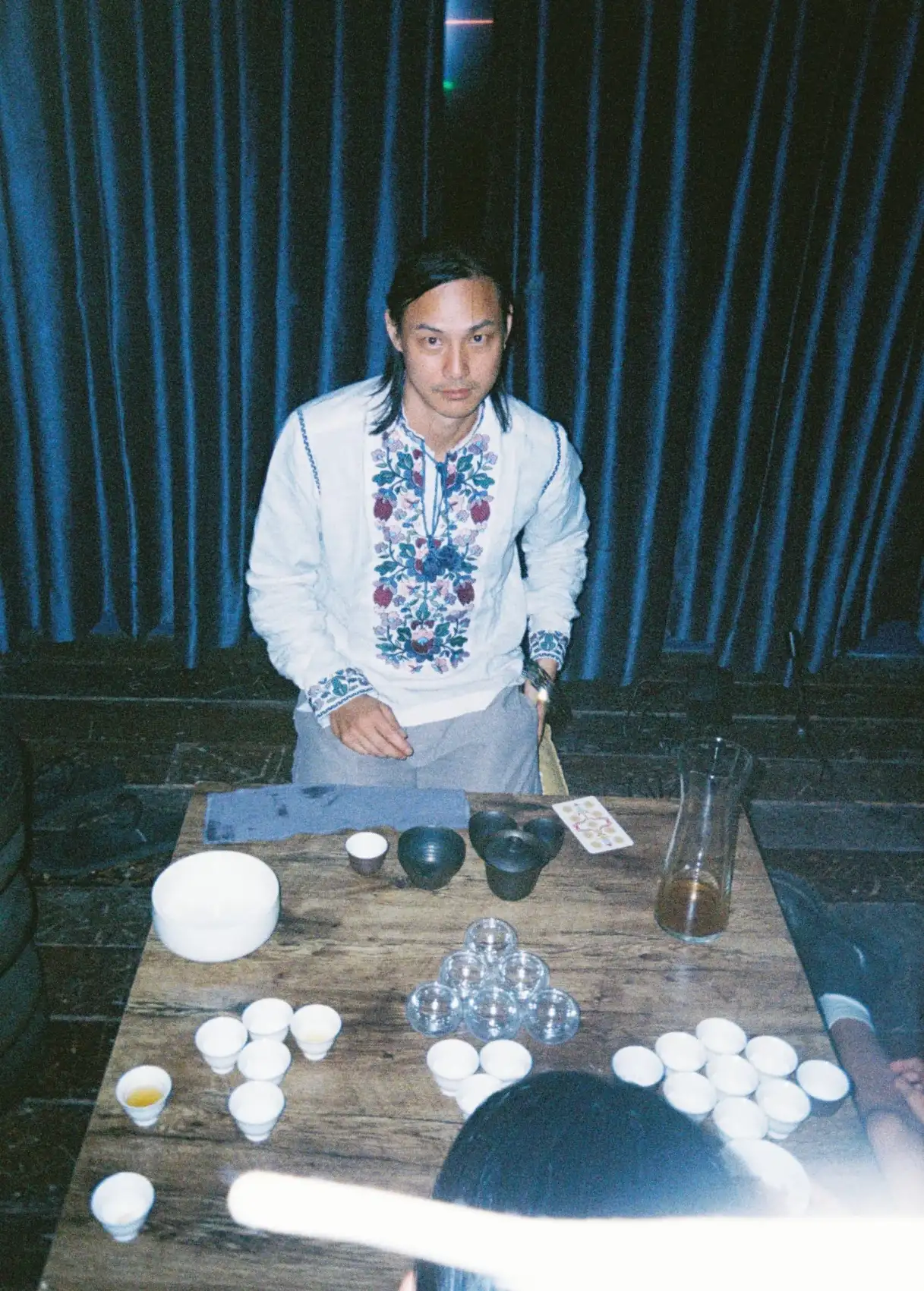 A very serious man glaring at the camera with many tea cups in front of him
